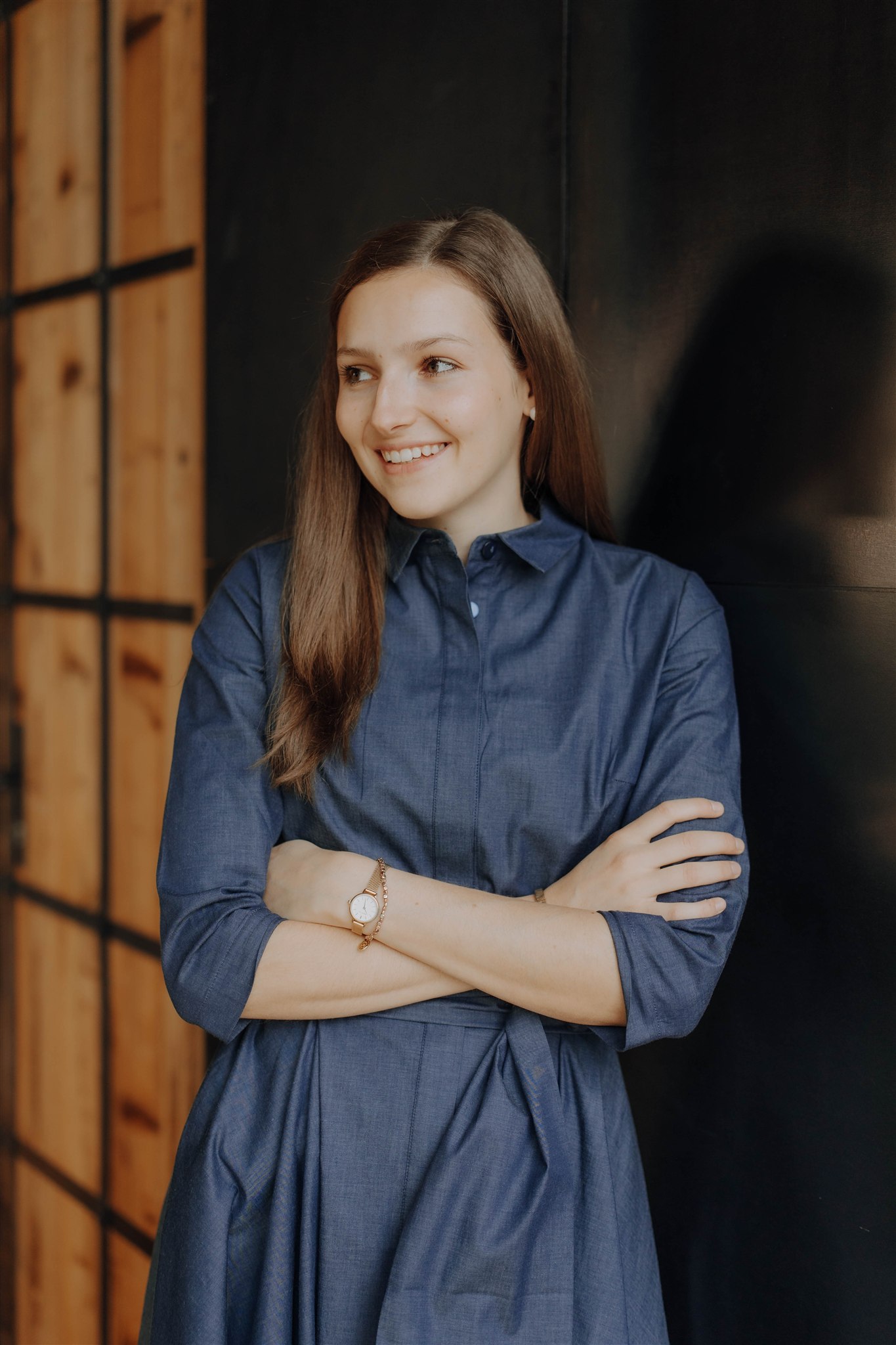 Woman in a blue blouse, smiling in front of a wooden wall